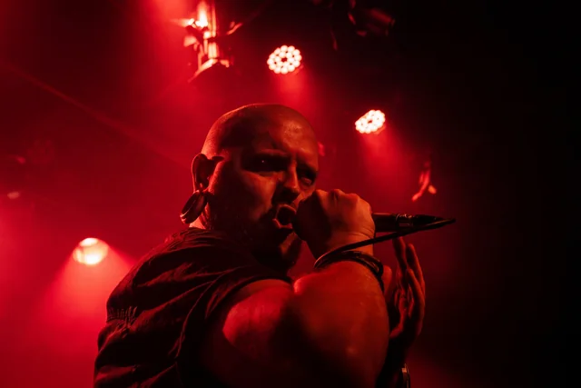 Nik Harchenko singing into a microphone beneath crimson lights